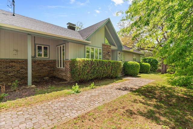 view of home's exterior featuring roof with shingles, a chimney, and brick siding