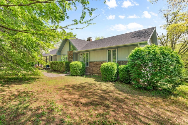 view of side of property with brick siding, roof with shingles, a yard, and a chimney