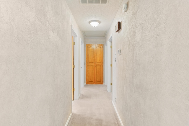 hallway featuring light colored carpet, a textured ceiling, baseboards, and visible vents