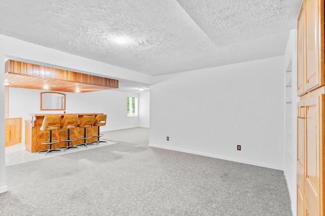 below grade area with a textured ceiling, bar, and carpet
