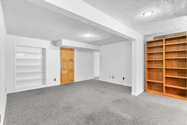 finished below grade area featuring baseboards, carpet, a textured ceiling, and built in shelves