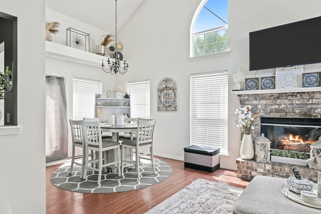 dining area with wood finished floors, a fireplace, baseboards, high vaulted ceiling, and a chandelier