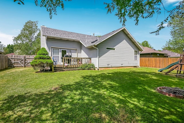 rear view of property with roof with shingles, a lawn, a wooden deck, a fenced backyard, and a playground