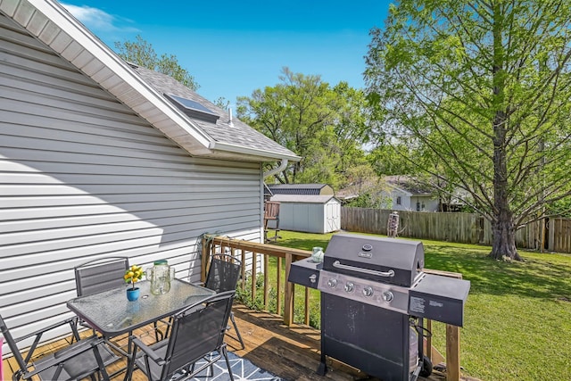 wooden terrace with outdoor dining space, a shed, a fenced backyard, a lawn, and a grill