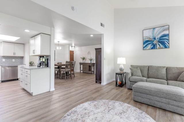 living room featuring a high ceiling, light wood finished floors, recessed lighting, baseboards, and visible vents