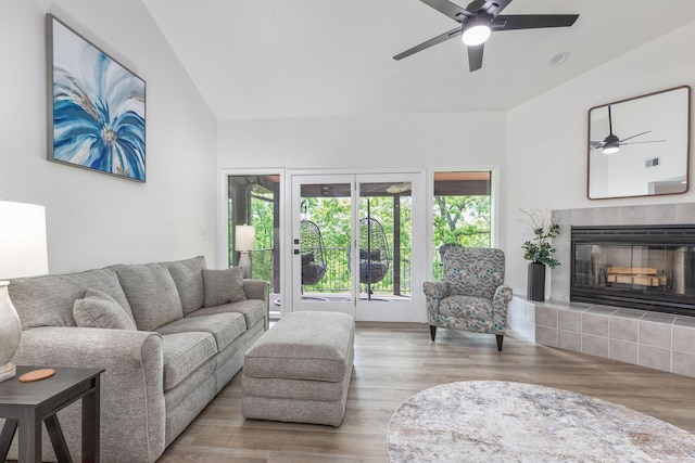 living area featuring a ceiling fan, vaulted ceiling, a tile fireplace, and wood finished floors