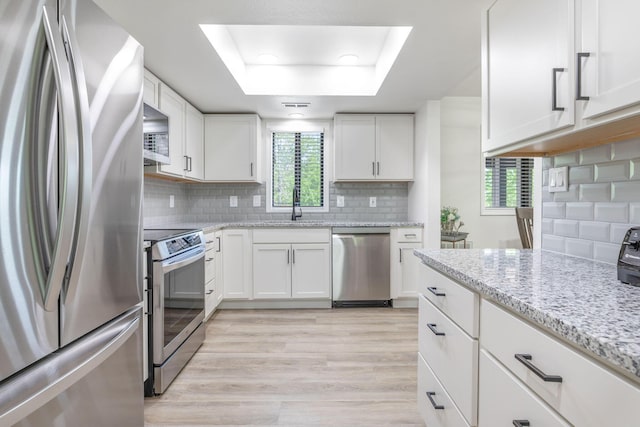 kitchen featuring white cabinets, a sink, a raised ceiling, stainless steel appliances, and decorative backsplash
