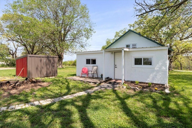 back of house featuring a yard, an outbuilding, and stucco siding