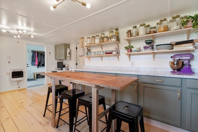 kitchen with light wood-style floors, a kitchen bar, open shelves, gray cabinetry, and heating unit