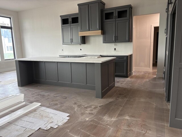 kitchen featuring glass insert cabinets, baseboards, a kitchen island, and light countertops