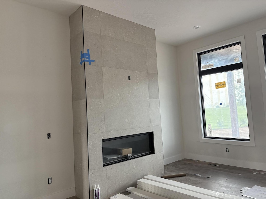unfurnished living room with baseboards, wood finished floors, a wealth of natural light, and a tile fireplace
