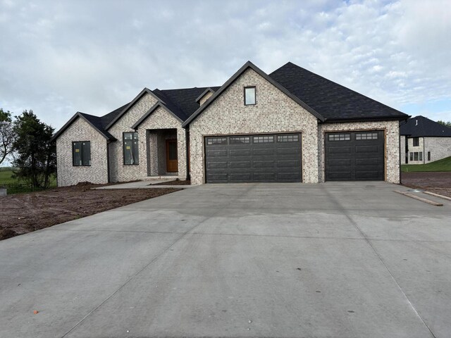 view of front of home with brick siding, an attached garage, driveway, and a shingled roof