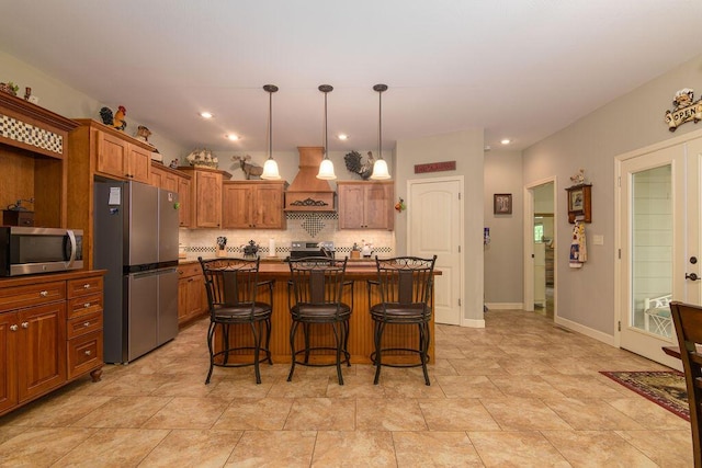 kitchen featuring brown cabinets, a breakfast bar, stainless steel appliances, custom range hood, and backsplash