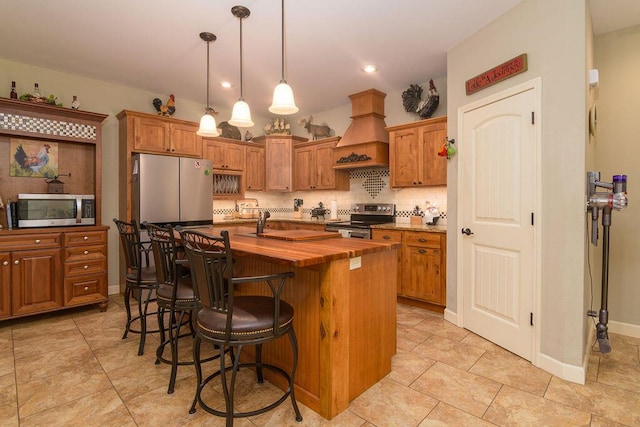 kitchen featuring decorative backsplash, butcher block counters, custom exhaust hood, a center island with sink, and appliances with stainless steel finishes