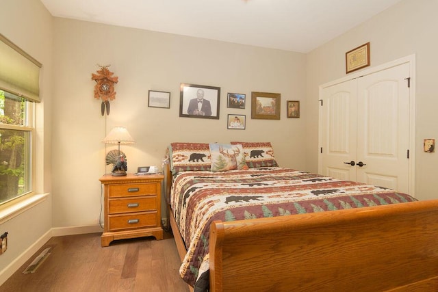 bedroom featuring baseboards, visible vents, wood finished floors, and a closet