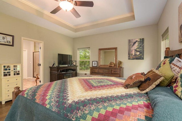 bedroom featuring a raised ceiling, ornamental molding, a ceiling fan, and wood finished floors