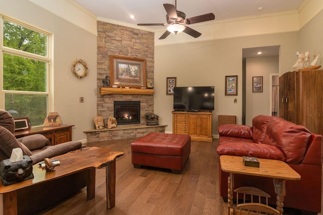 living area with crown molding, ceiling fan, a stone fireplace, and wood finished floors