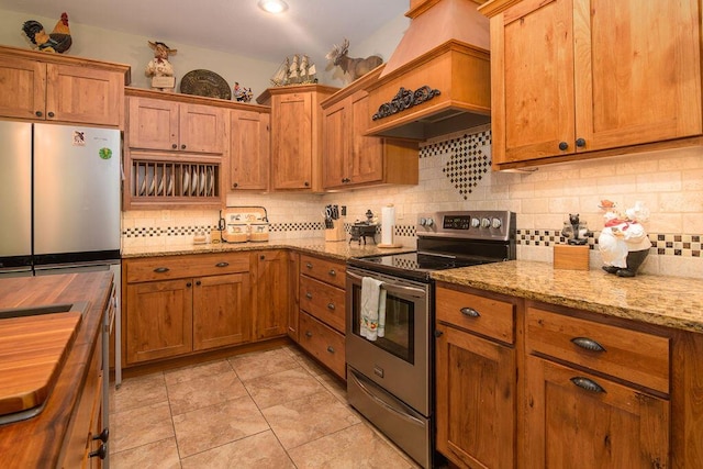 kitchen with appliances with stainless steel finishes, tasteful backsplash, brown cabinetry, and wooden counters