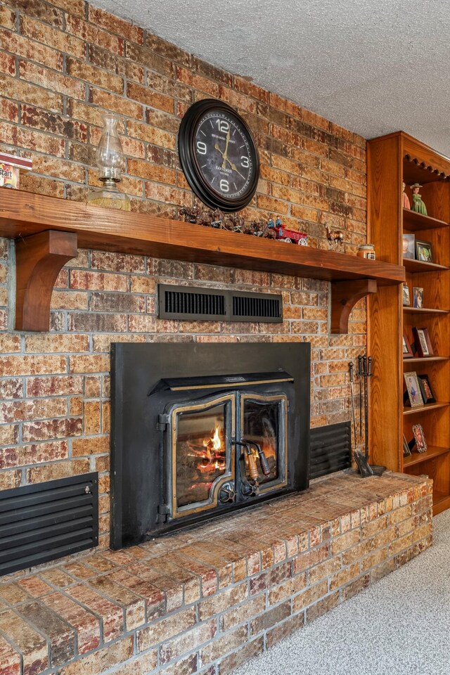 interior details featuring visible vents, carpet, a textured ceiling, and a glass covered fireplace