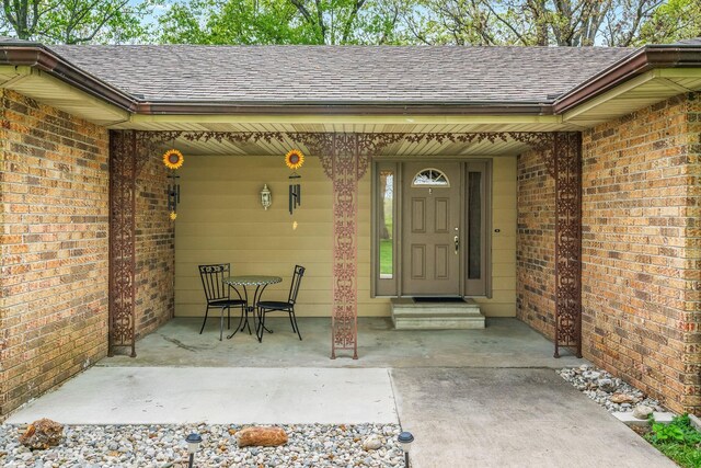 doorway to property featuring roof with shingles and brick siding