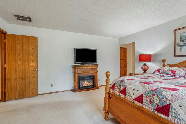 carpeted bedroom featuring visible vents, a textured ceiling, a glass covered fireplace, and baseboards