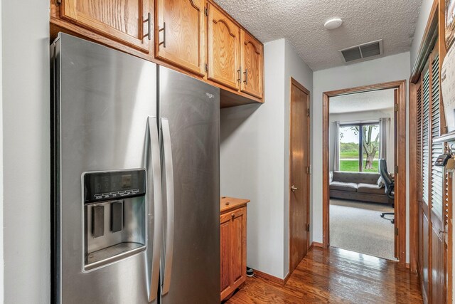kitchen with brown cabinetry, visible vents, wood finished floors, stainless steel refrigerator with ice dispenser, and a textured ceiling