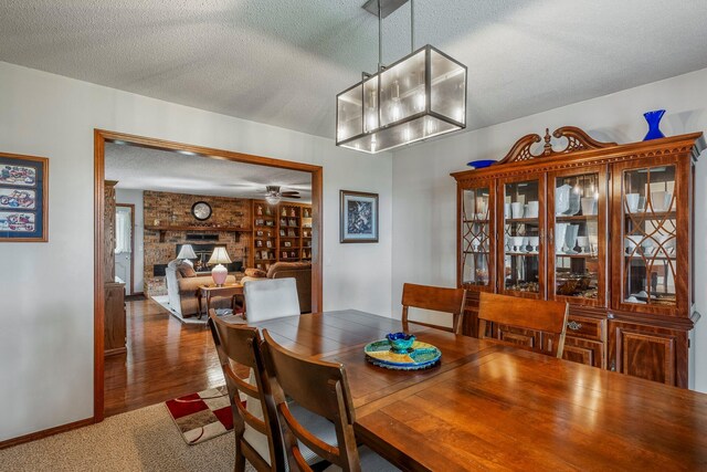 dining room with a brick fireplace, a textured ceiling, a ceiling fan, baseboards, and wood finished floors