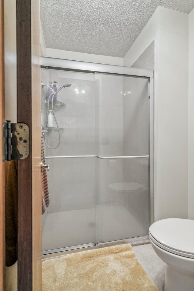 full bathroom featuring a shower stall, toilet, and a textured ceiling