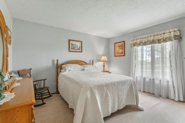 bedroom featuring visible vents, a textured ceiling, and light colored carpet