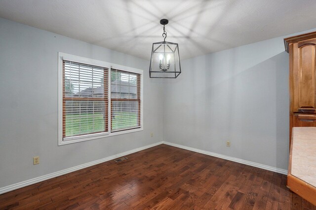 empty room featuring visible vents, dark wood-style flooring, baseboards, and a chandelier
