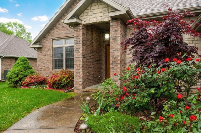 property entrance with a yard, brick siding, central AC, and roof with shingles