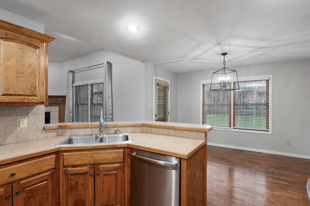 kitchen featuring tasteful backsplash, stainless steel dishwasher, a sink, a peninsula, and dark wood-type flooring