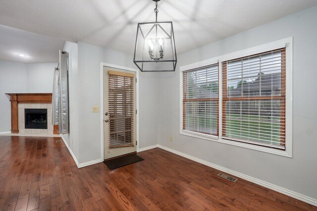 unfurnished dining area featuring a notable chandelier, a fireplace, baseboards, dark wood-type flooring, and visible vents