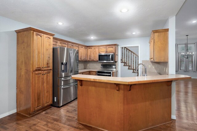 kitchen featuring appliances with stainless steel finishes, backsplash, a peninsula, and dark wood-style floors