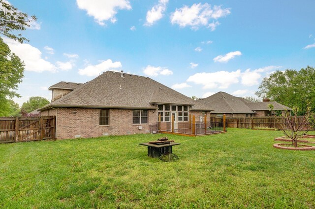 back of house with roof with shingles, brick siding, a fenced backyard, a yard, and a fire pit