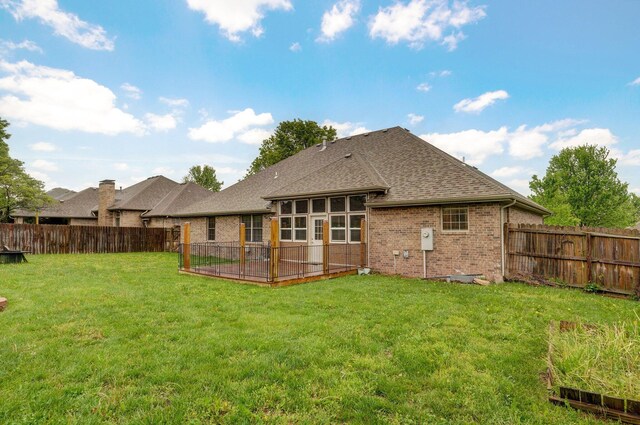 rear view of property featuring a yard, brick siding, a fenced backyard, and roof with shingles