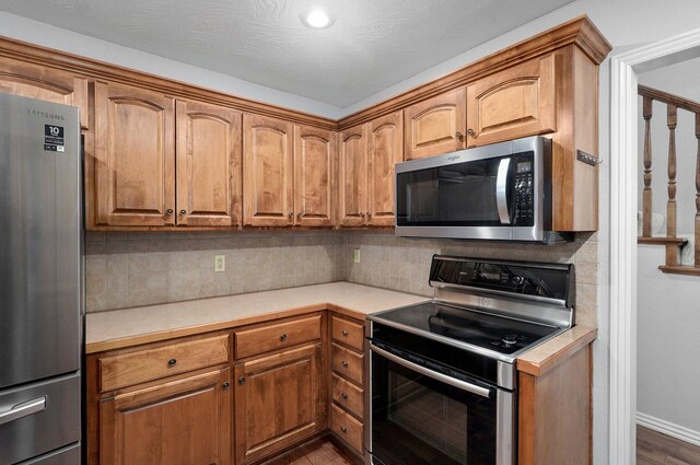 kitchen featuring light countertops, appliances with stainless steel finishes, tasteful backsplash, and brown cabinetry