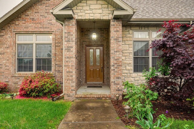 property entrance with roof with shingles, stone siding, and brick siding