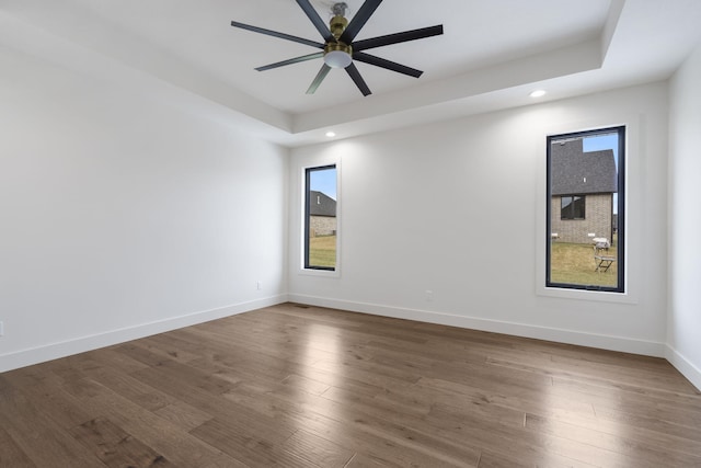 empty room featuring dark wood-style flooring, ceiling fan, recessed lighting, baseboards, and a tray ceiling