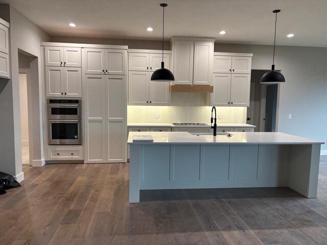 kitchen with a center island with sink, a sink, light countertops, double oven, and dark wood-style floors