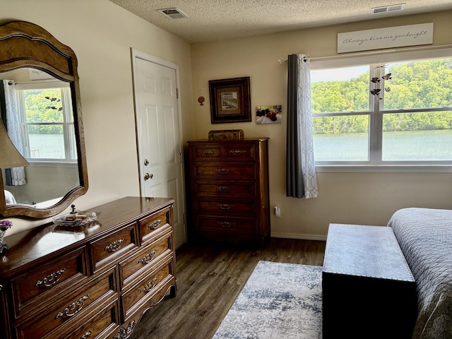 bedroom with baseboards, a textured ceiling, visible vents, and dark wood finished floors