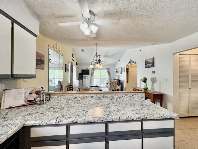 kitchen featuring light stone counters, a textured ceiling, ceiling fan with notable chandelier, a peninsula, and vaulted ceiling