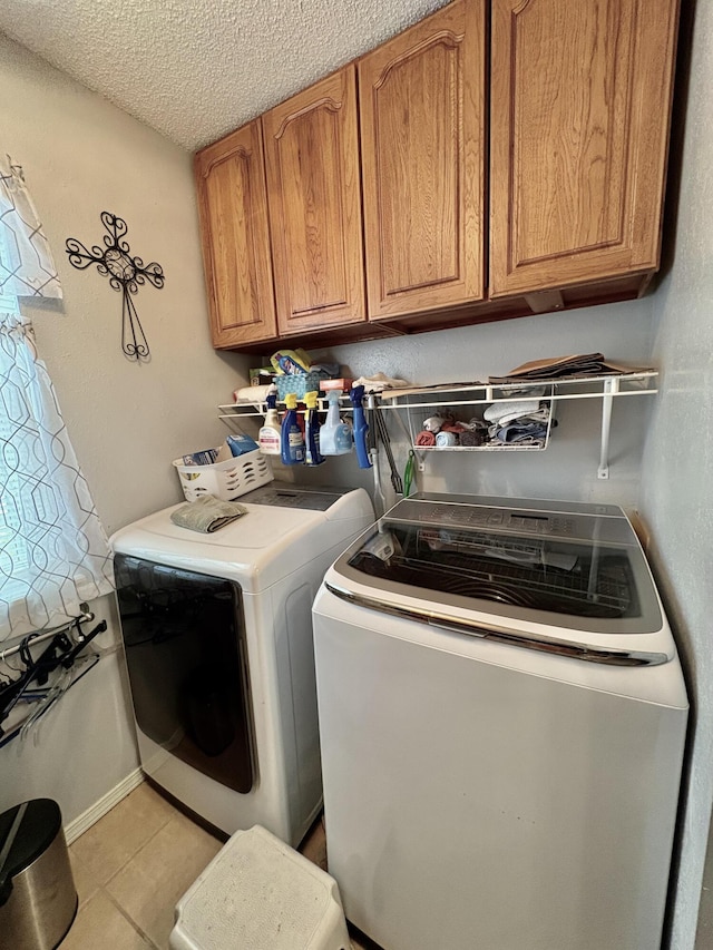 clothes washing area featuring light tile patterned floors, a textured ceiling, cabinet space, and washing machine and clothes dryer