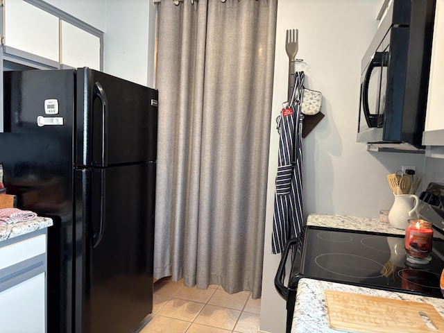 kitchen with white cabinets, black appliances, and light tile patterned flooring