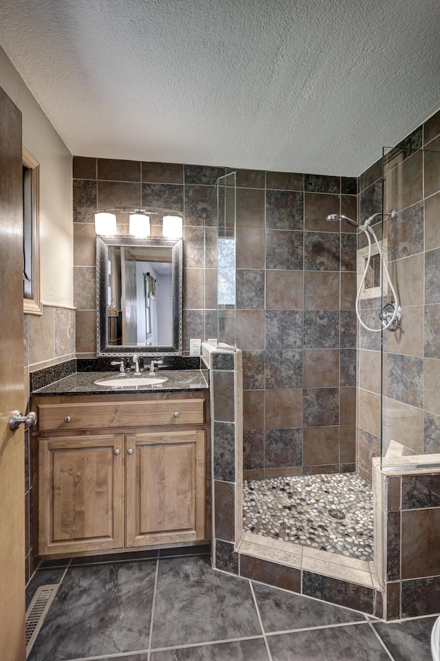 bathroom with vanity, a textured ceiling, a tile shower, and tile walls