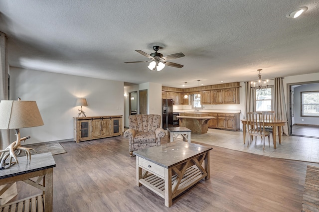 living area with baseboards, ceiling fan with notable chandelier, light wood finished floors, and a textured ceiling