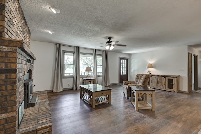 living room with ceiling fan, a textured ceiling, a fireplace, wood finished floors, and baseboards