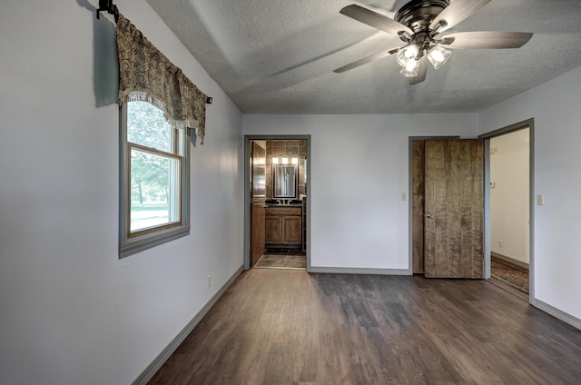 unfurnished bedroom with ceiling fan, a textured ceiling, wood finished floors, baseboards, and ensuite bathroom