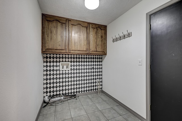 laundry room with baseboards, a textured ceiling, cabinet space, and light tile patterned flooring