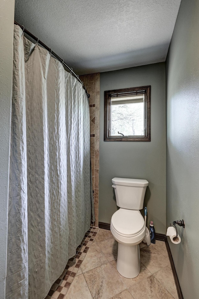 full bathroom featuring baseboards, toilet, and a textured ceiling